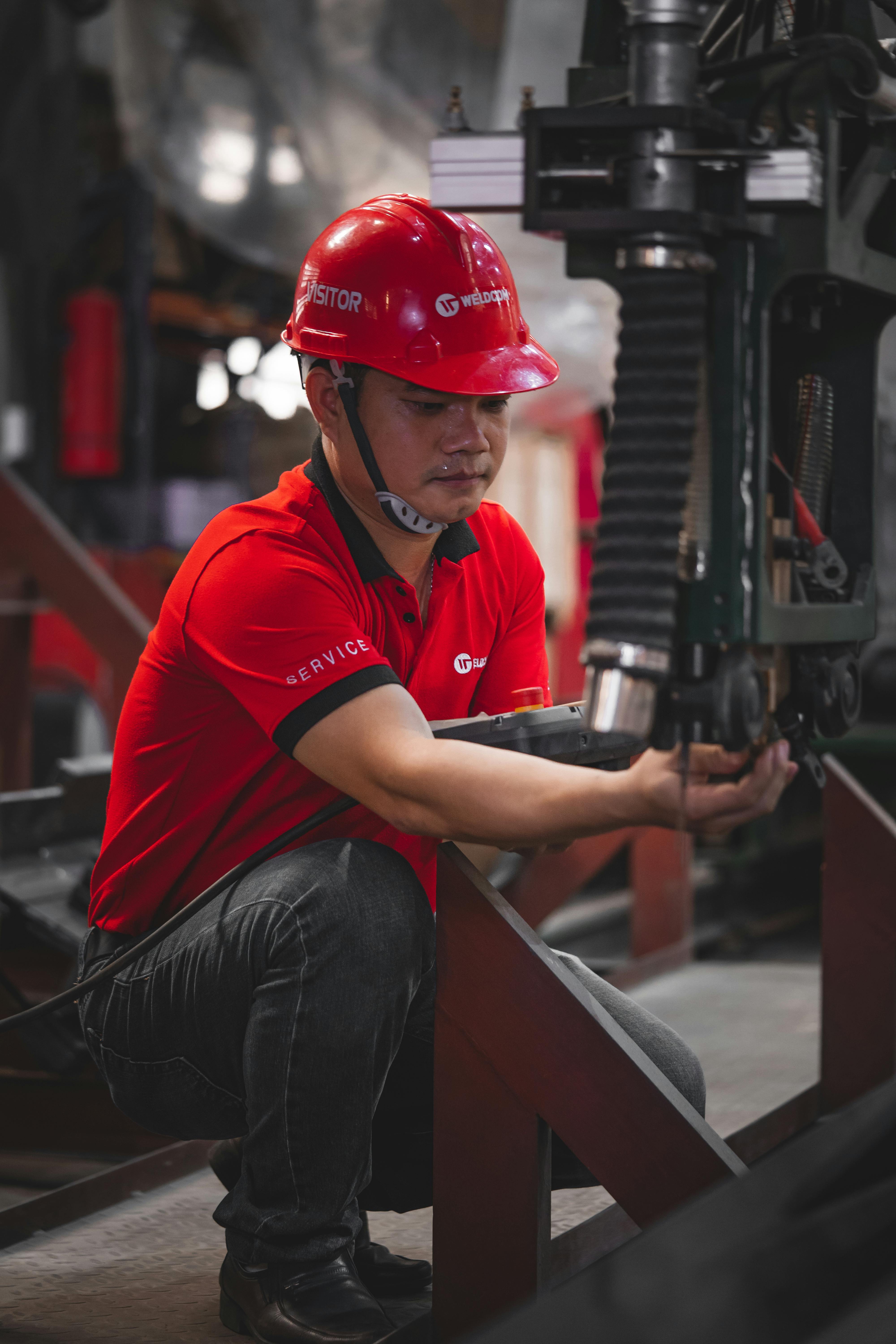 Worker in a red safety helmet and red shirt operating industrial machinery in a workshop.
