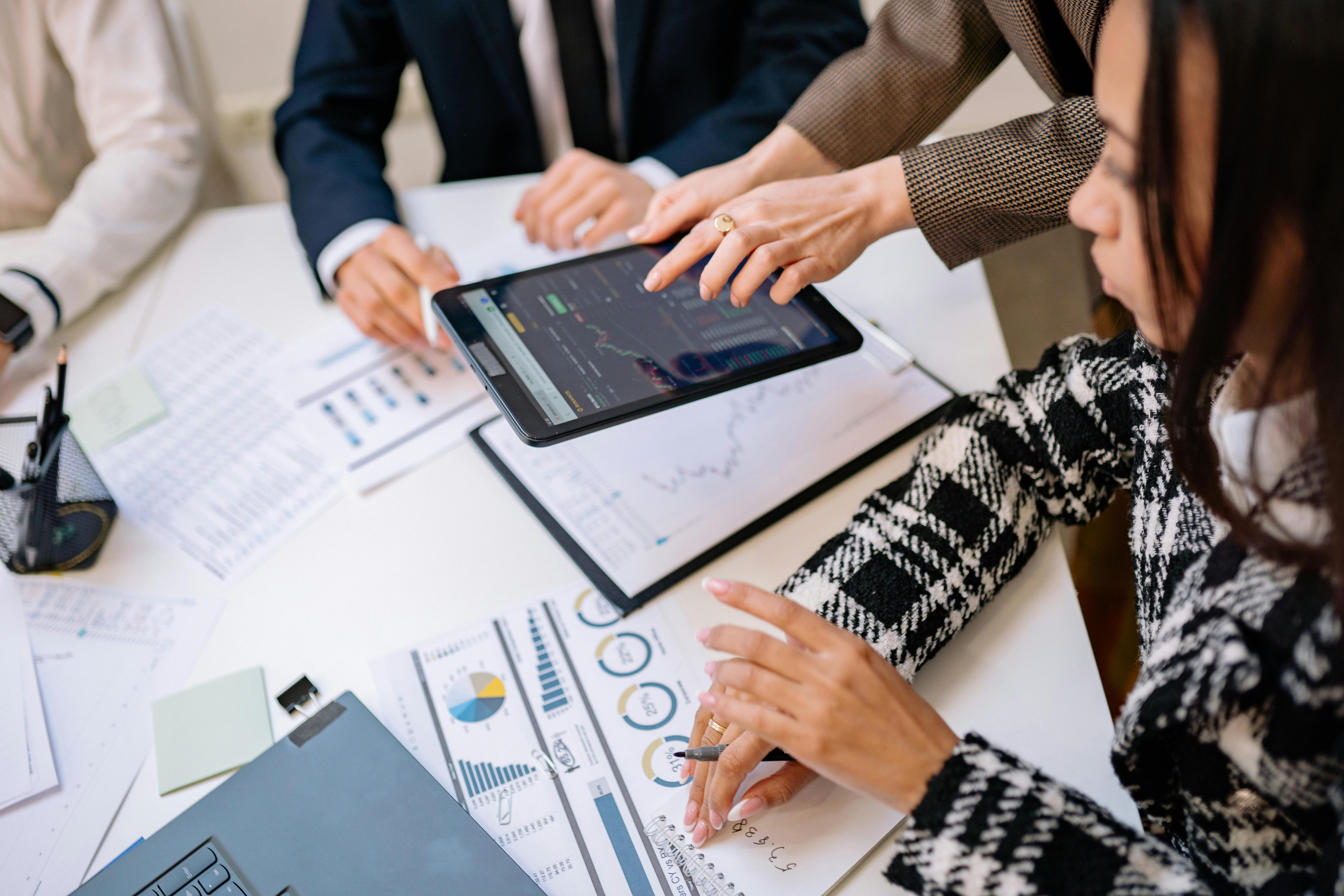 Three professionals reviewing financial charts and graphs with a tablet and documents on a white table.