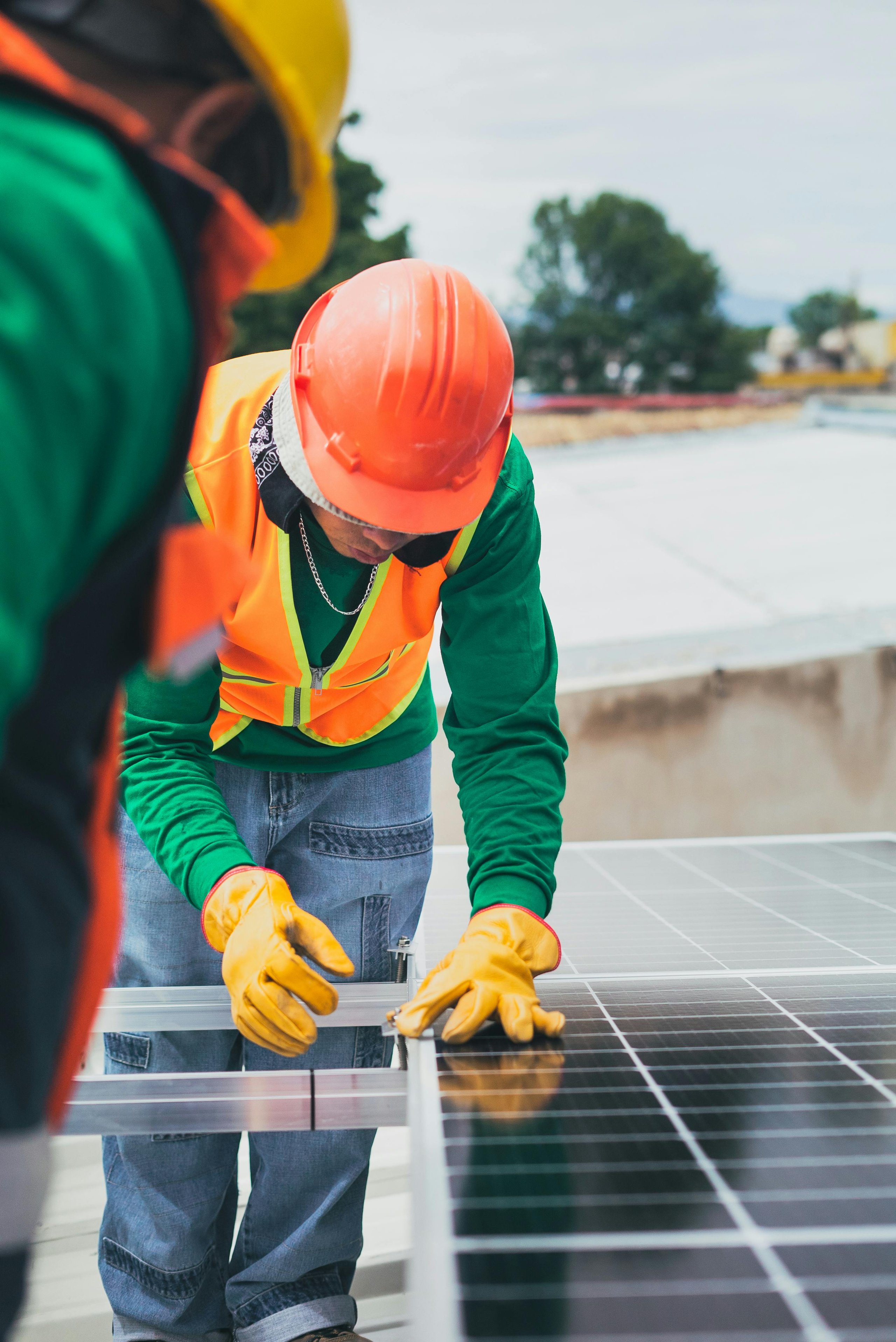 Two construction workers in safety gear installing solar panels on a rooftop.